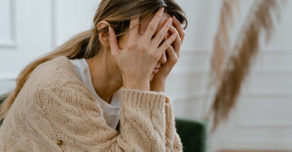 A woman sitting indoors covering her face in frustration, depicting stress and mental health challenges.